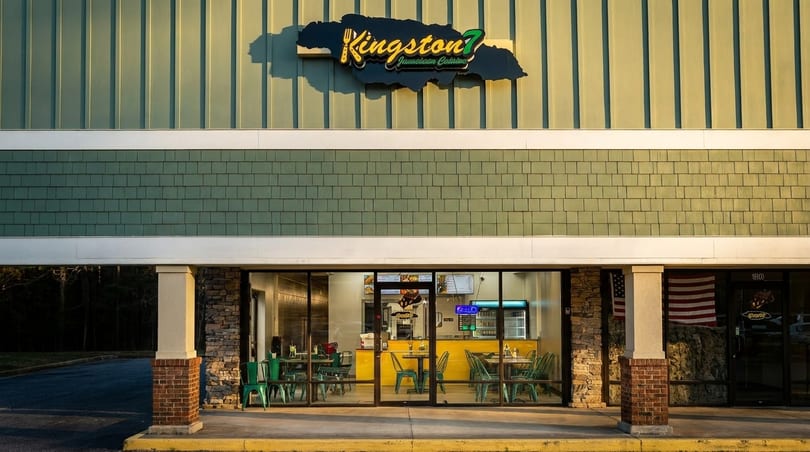 Exterior of Kingston 7 Jamaican Cuisine restaurant with green siding and a bright yellow interior.