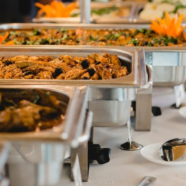 Buffet line with several chafing dishes filled with various hot dishes and serving spoons.