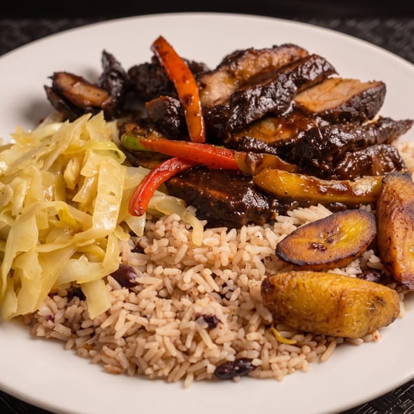 A plate of Jamaican jerk pork with rice and peas, steamed cabbage, and fried plantains.