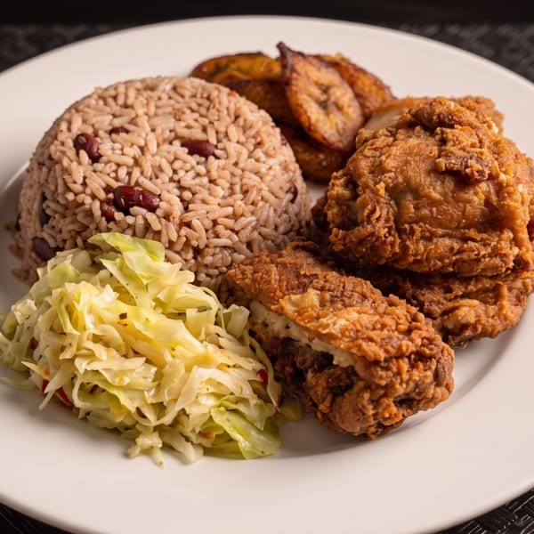 Fried chicken, rice and peas, plantains, and cabbage on a white plate.