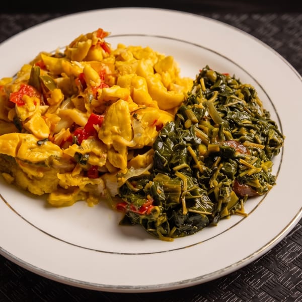 A plate of Jamaican ackee and saltfish with callaloo, and a fork on a dark placemat.