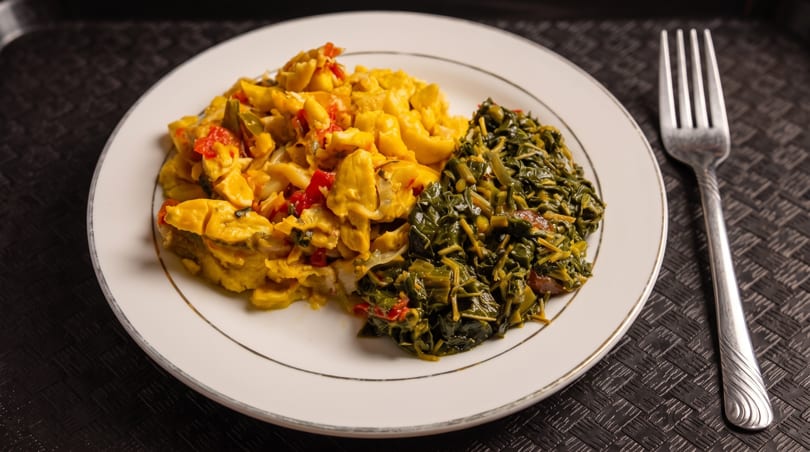 A plate of Jamaican ackee and saltfish with callaloo, and a fork on a dark placemat.